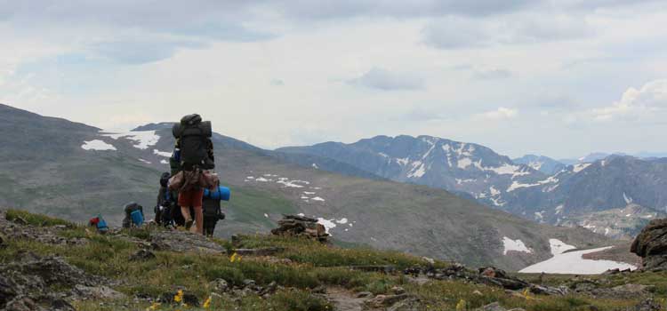a group of people backpacking in the mountains during summer camp family trips