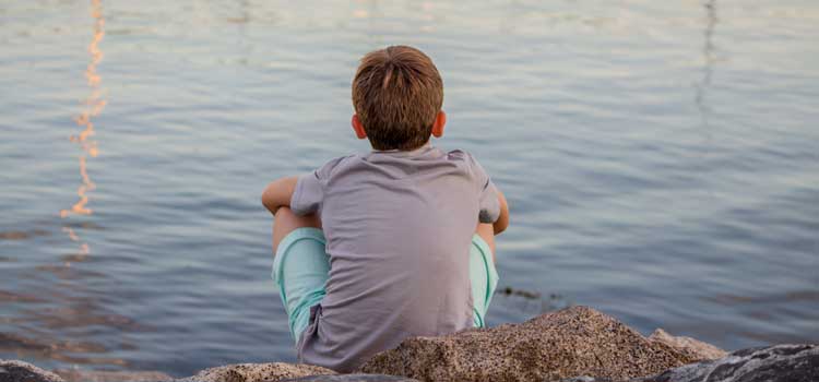 kid sitting alone looking at a lake