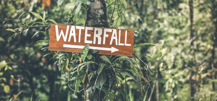 a wooden sign pointing to a waterfall