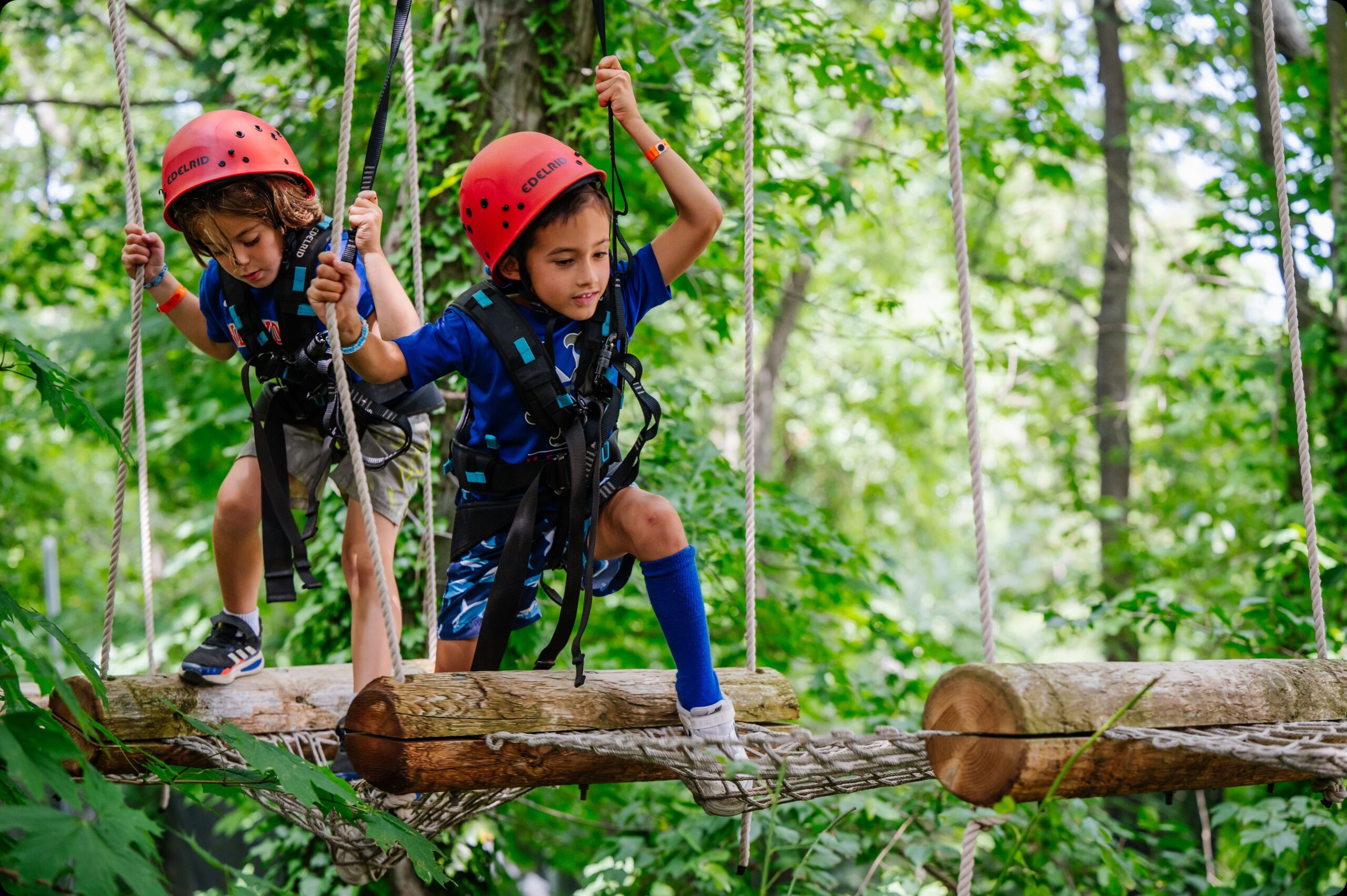 Two summer campers on a rope course in trees with helmets on